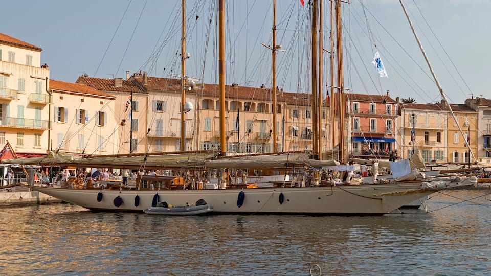 A historic waterfront with tall sailing ships docked, surrounded by colorful buildings and a crowd of people.