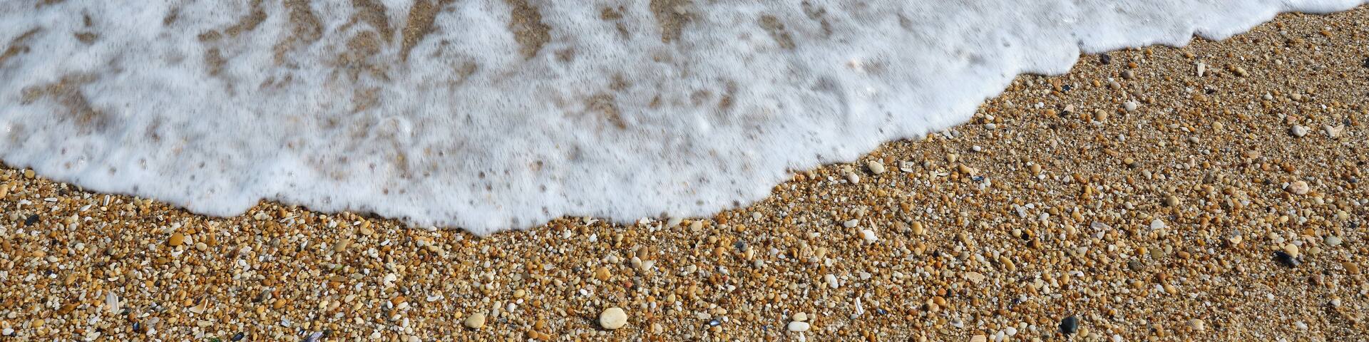 Small smooth pebbles and worn glass line the beach at low tide in the coastal community of Sea Girt New Jersey on the Atlantic Coast as small foamy waves wash over them