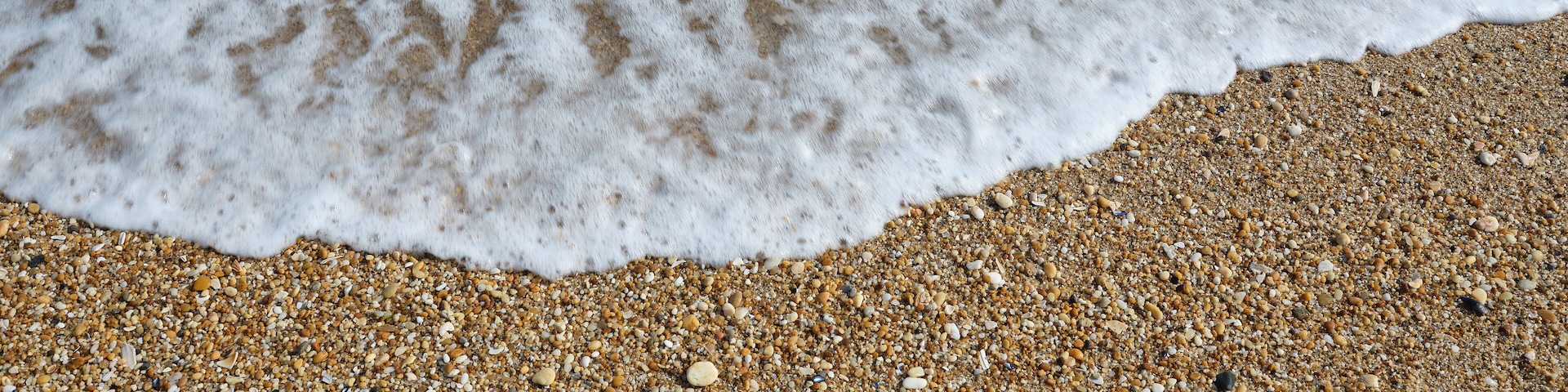Small smooth pebbles and worn glass line the beach at low tide in the coastal community of Sea Girt New Jersey on the Atlantic Coast as small foamy waves wash over them