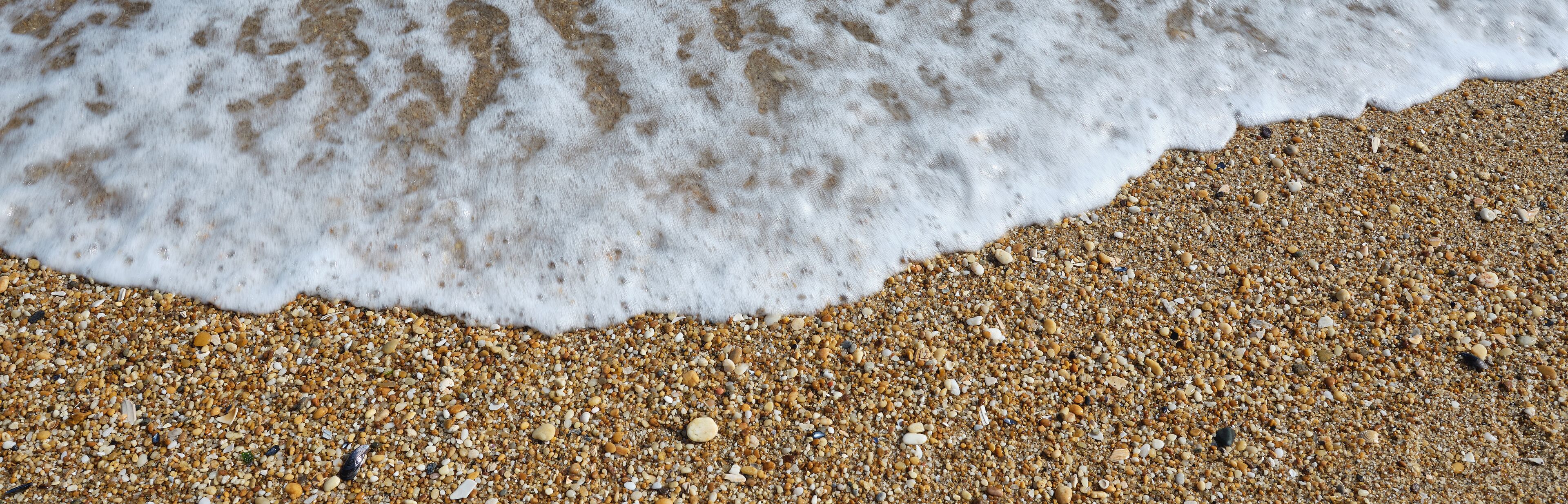 A sandy beach with small pebbles and a foamy wave.