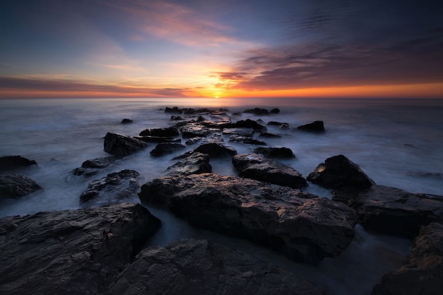 A rocky shoreline with a sunset in the background.