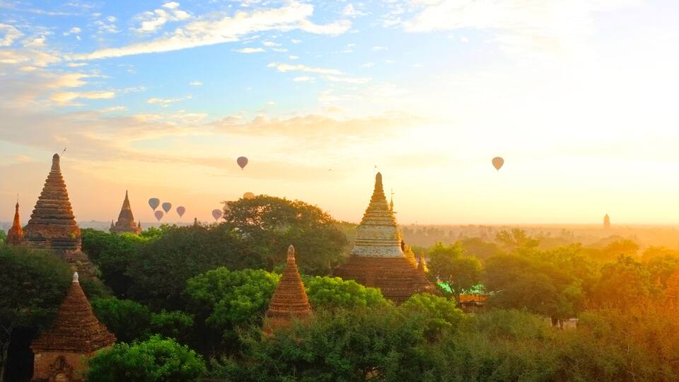 A landscape with multiple pagoda-style structures surrounded by lush greenery, with hot air balloons in the sky.