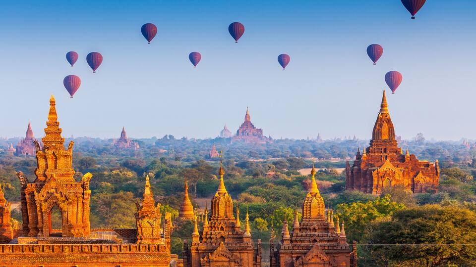 Ancient temples with golden spires, surrounded by lush greenery and hot air balloons in the sky.