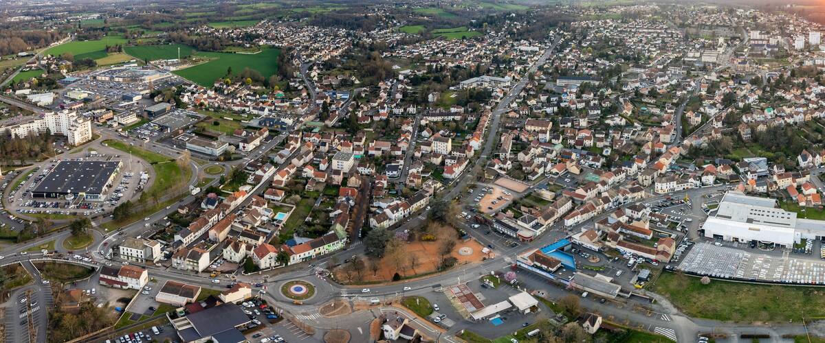 An aerial view of a town with a central roundabout, residential areas, and a large industrial building.