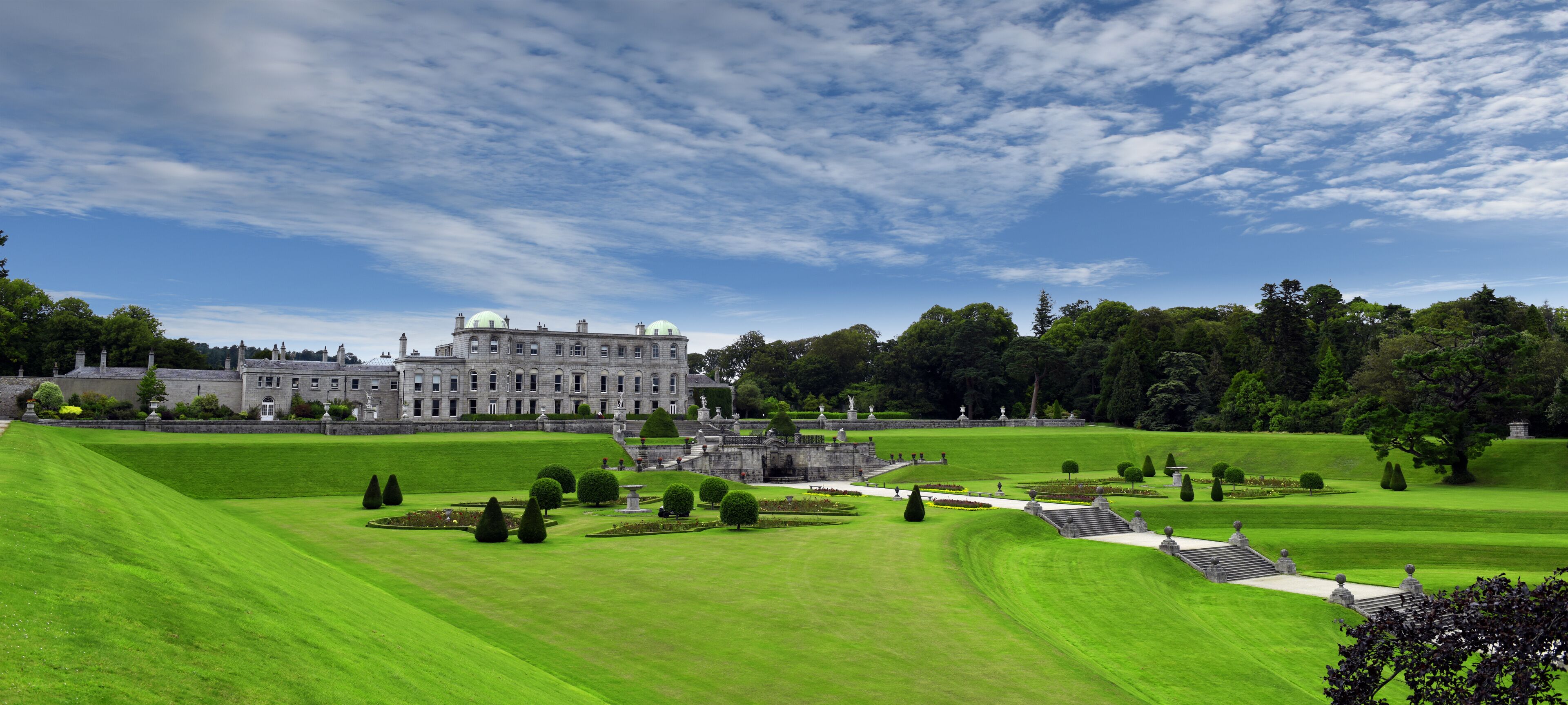 A large, historic building with a well-manicured lawn and statues in the foreground.