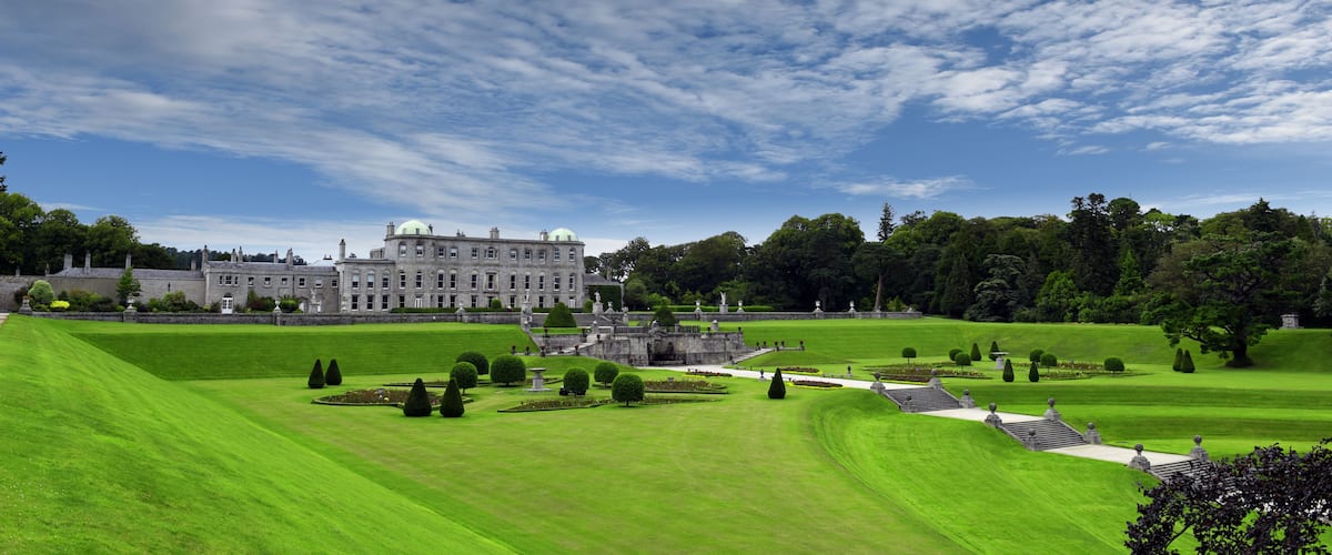 A large, historic building with a well-manicured lawn and statues in the foreground.