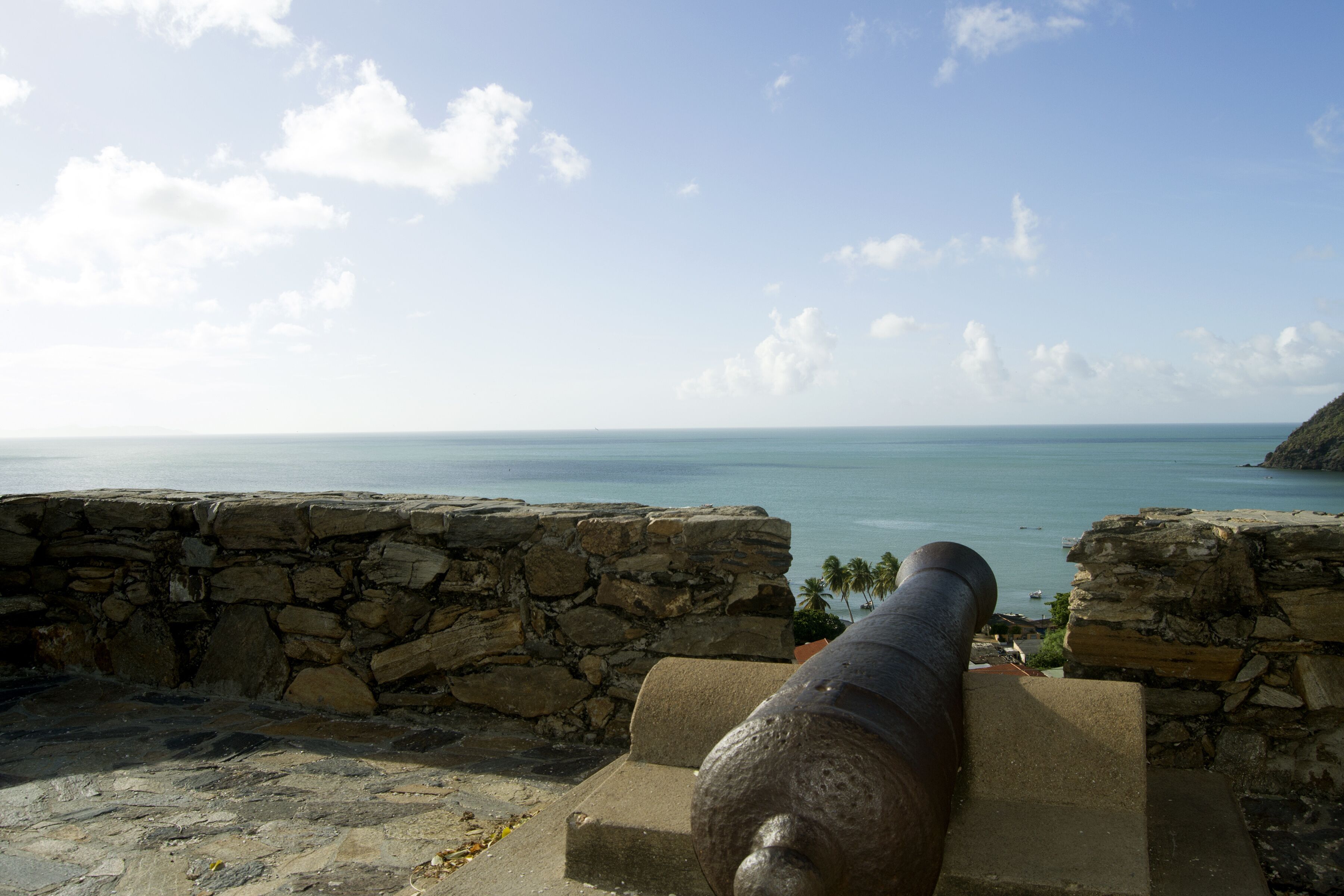 A cannon overlooking a coastal view with a stone wall and a clear sky.