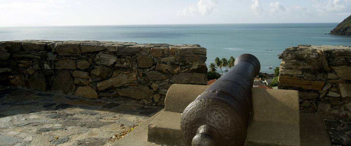 A cannon overlooking a coastal view with a stone wall and a clear sky.