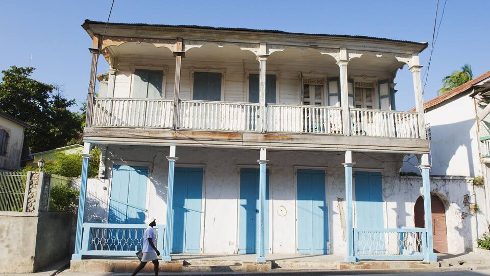 A two-story colonial-style building with blue doors and columns, a balcony, and a street in front.