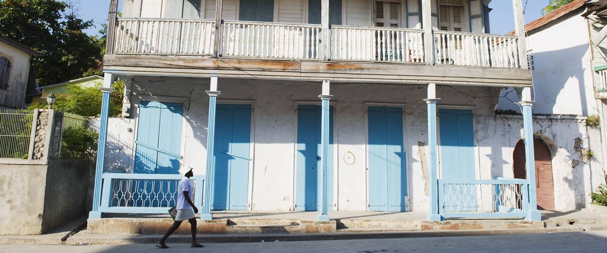 A two-story colonial-style building with blue doors and columns, a balcony, and a street in front.