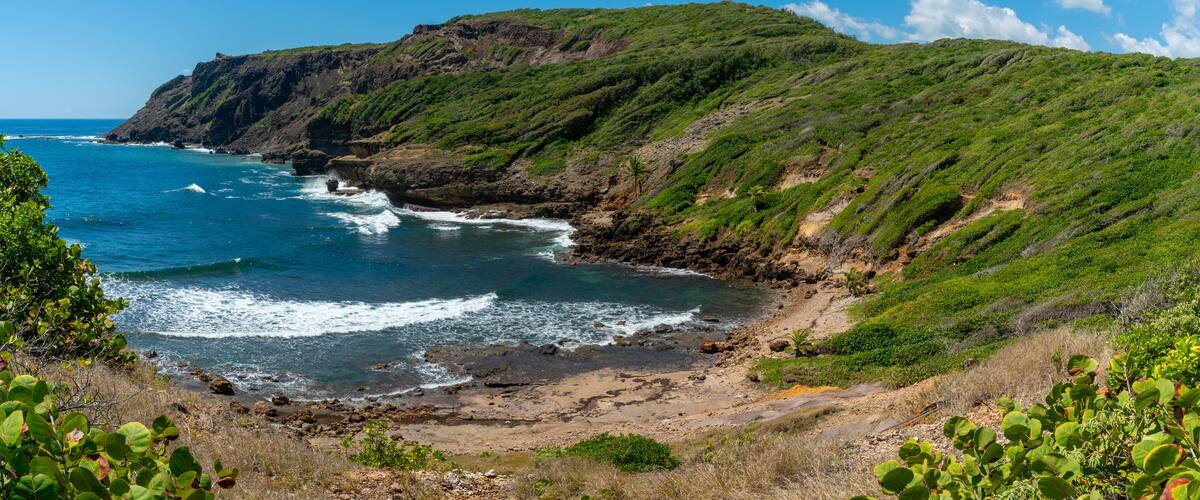 A coastal landscape with a rocky shoreline, green hills, and the ocean.