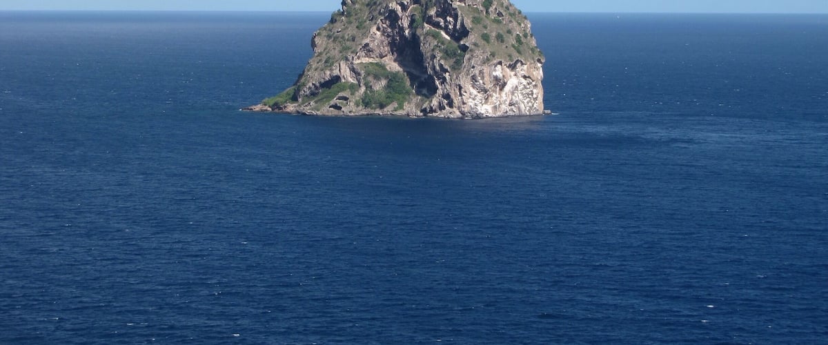 A small island with rocky terrain and sparse vegetation in the middle of a vast ocean.