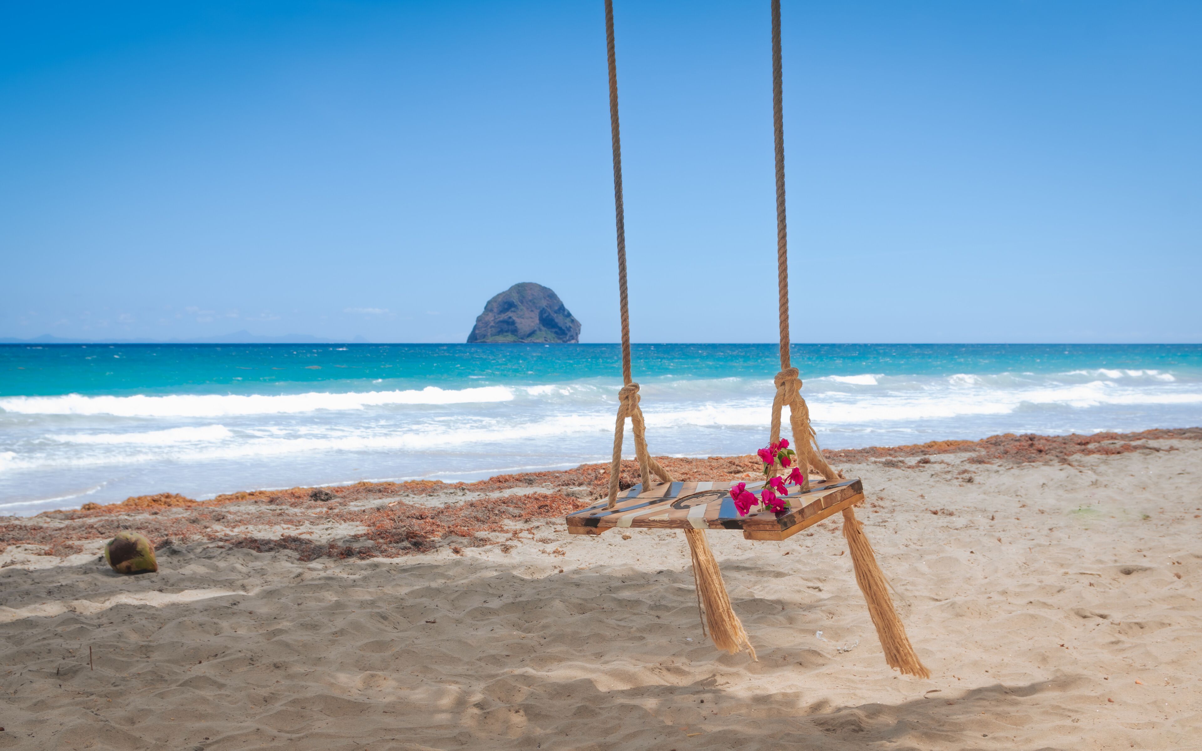 A beach with a swing set and a rock formation in the background.