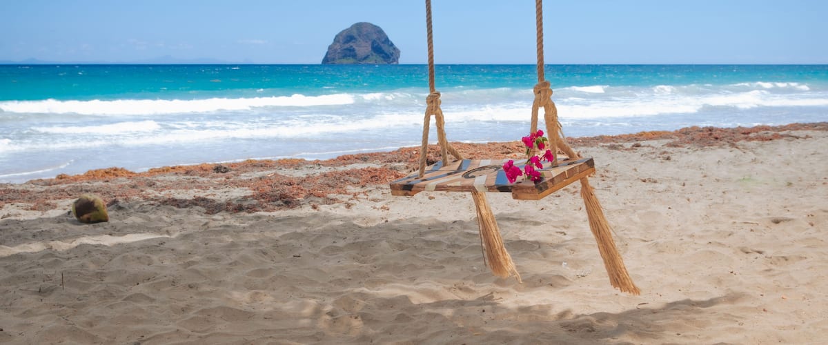 A beach with a swing set and a rock formation in the background.