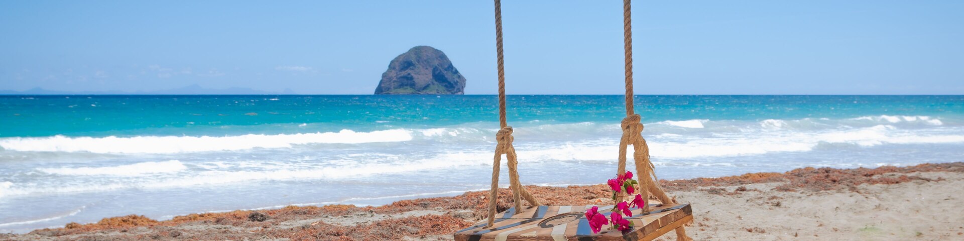 A beach with a swing set and a rock formation in the background.