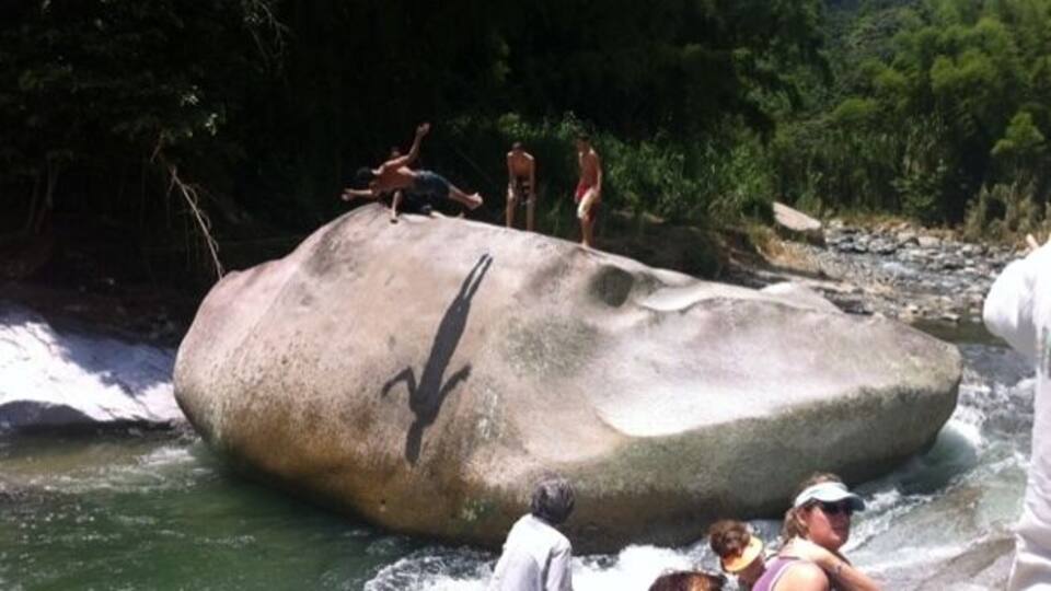 A large rock formation with people standing on it near a flowing river.