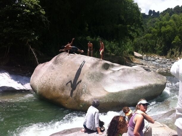 A large rock formation with people standing on it near a flowing river.