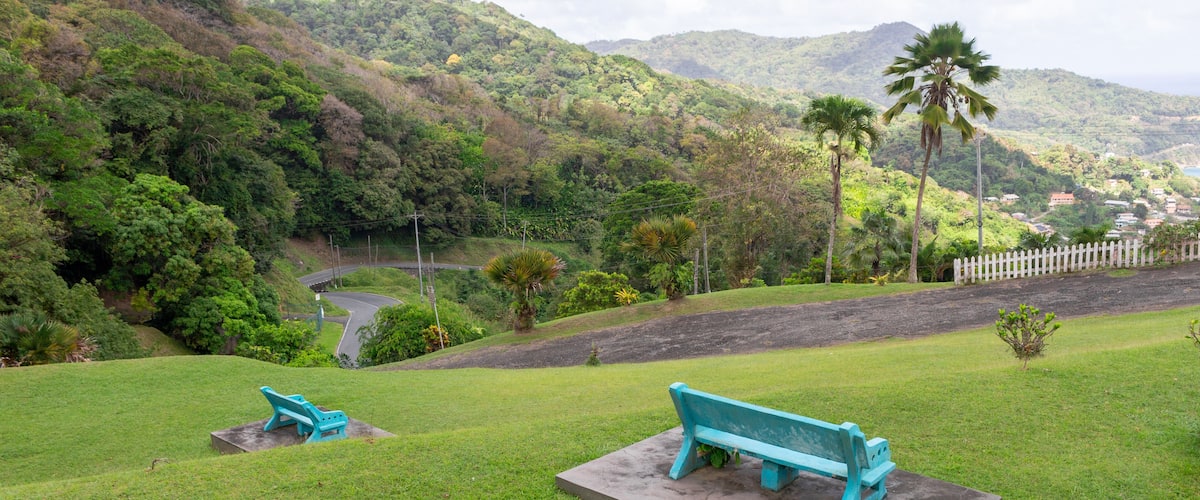 A park with two turquoise benches, lush green grass, and a white picket fence.