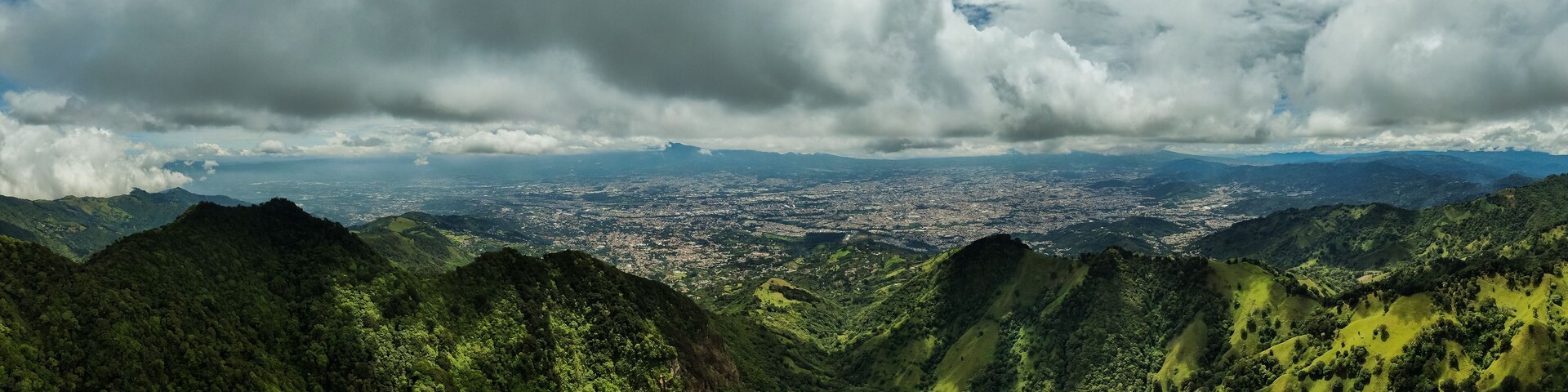 Paisagem montanhosa com florestas verdes densas e uma cidade no vale abaixo.