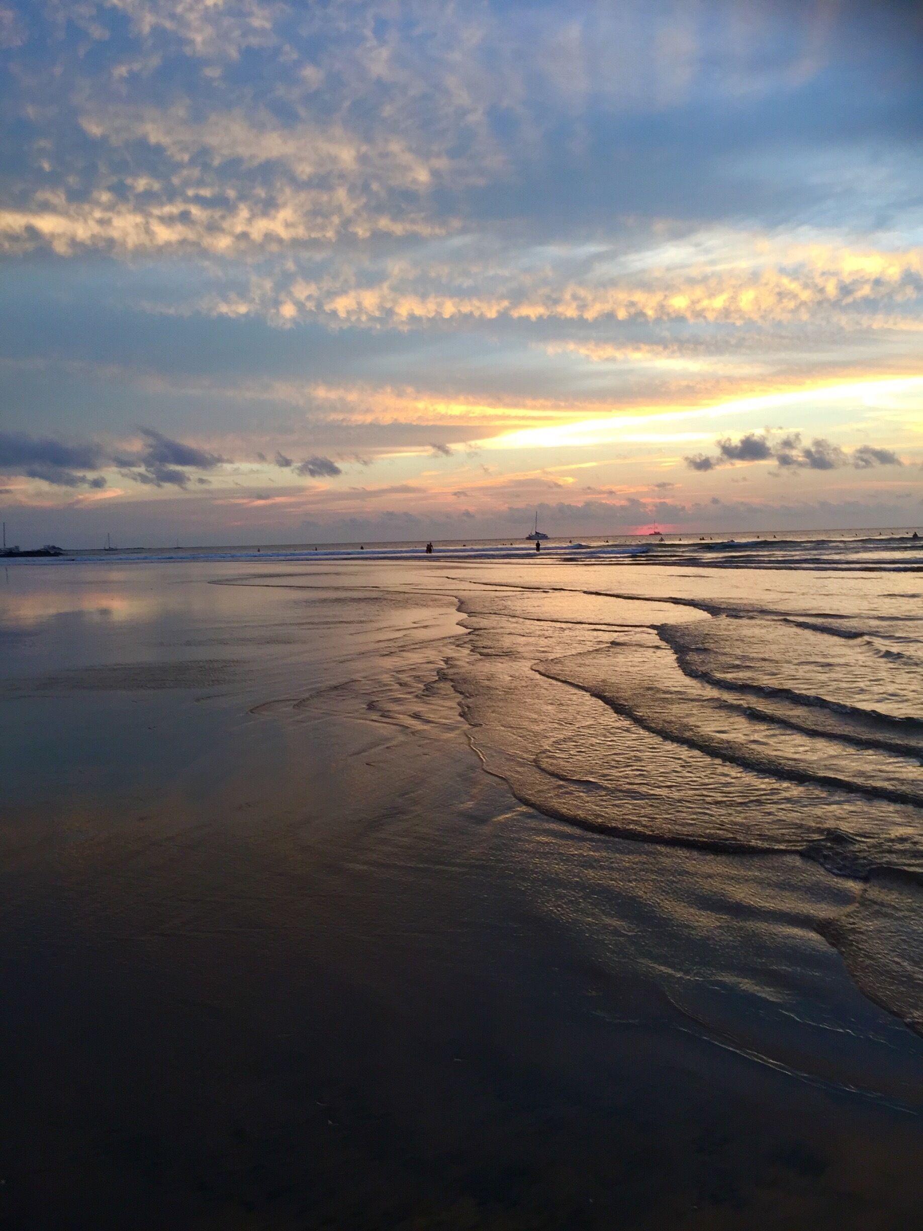 A beach with wet sand and gentle waves at sunset.