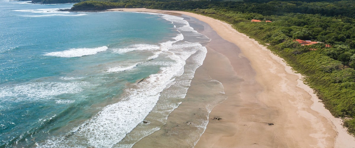 A beach with clear blue waters, a sandy shore, and green hills in the background.