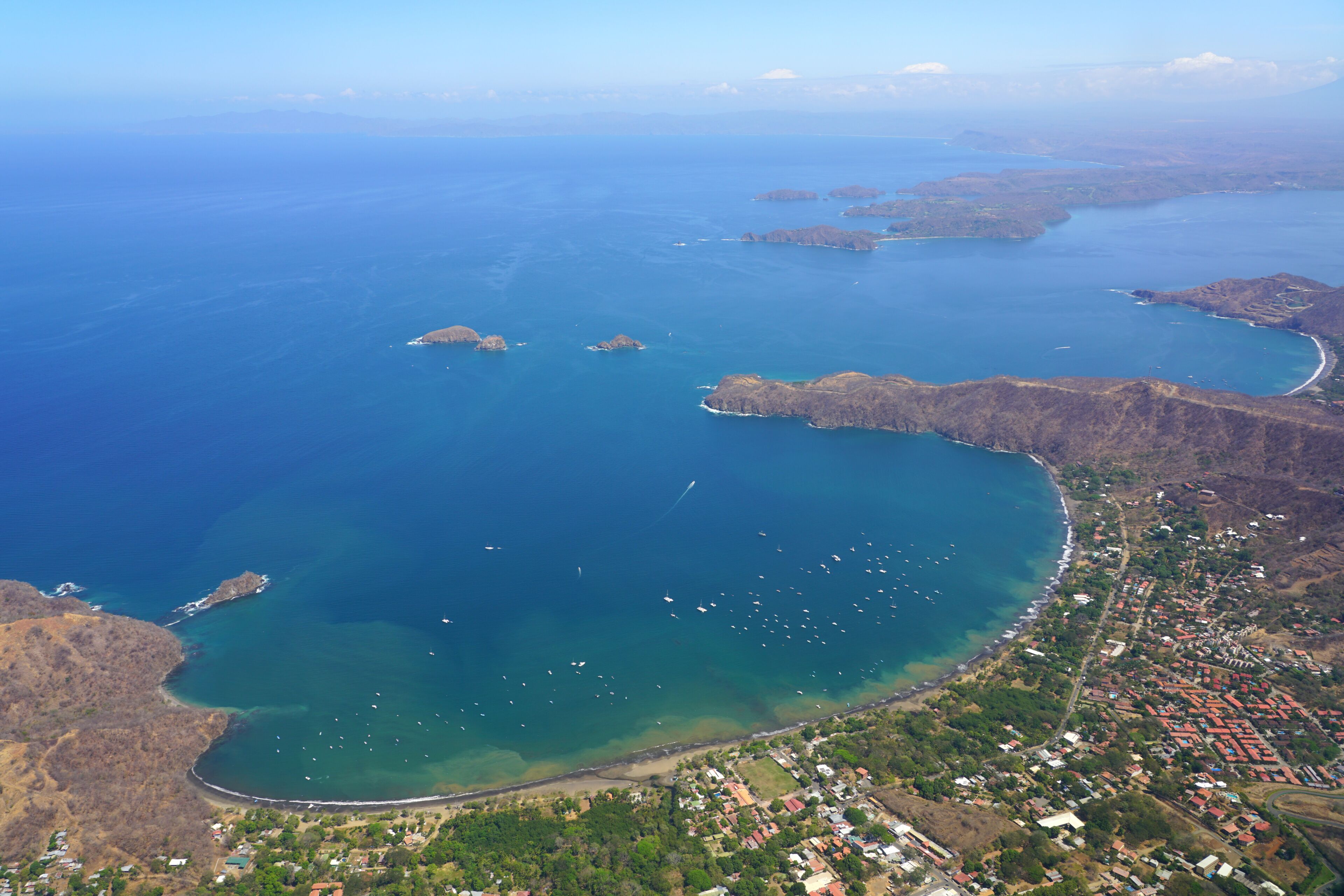 An aerial view of a coastal town with a bay, clear waters, and scattered islands.