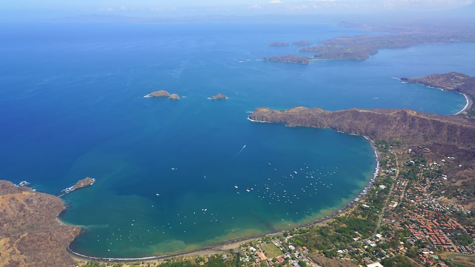 An aerial view of a coastal town with a bay, clear waters, and scattered islands.