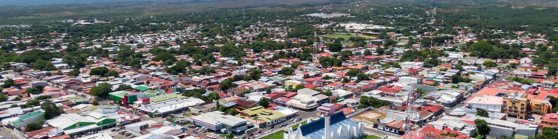 An aerial view of a city with a mix of residential and commercial buildings, a prominent white church, and a mountain range in the background.