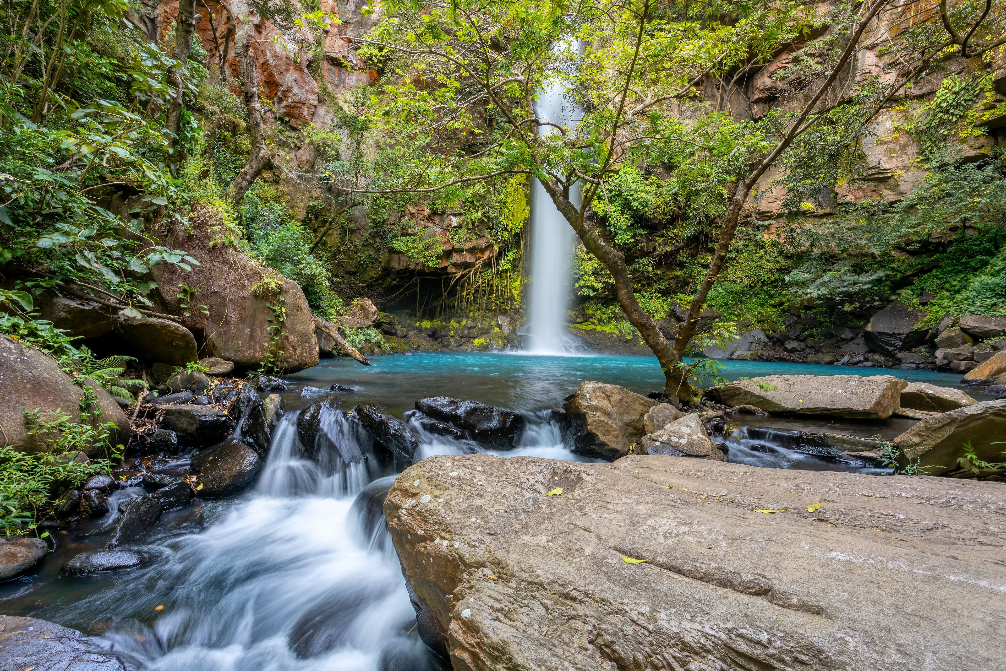 A waterfall cascading into a turquoise pool surrounded by rocks and lush greenery.