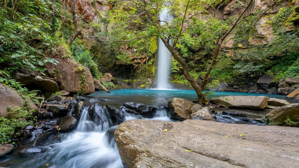 A waterfall cascading into a turquoise pool surrounded by rocks and lush greenery.