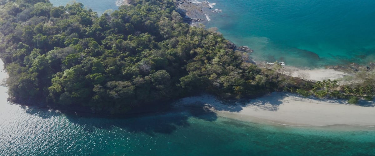 An aerial view of a tropical island with a sandy beach and clear turquoise waters.