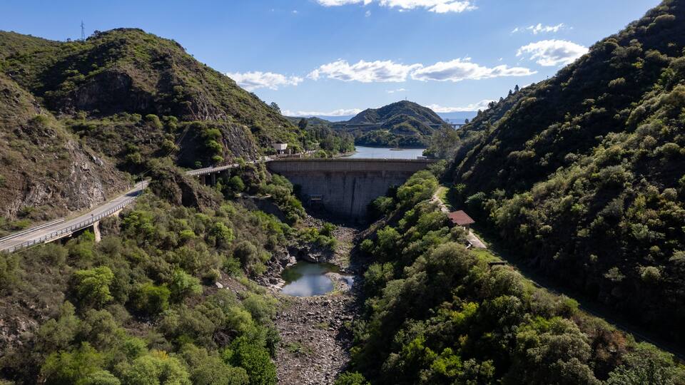 A bridge over a river, surrounded by lush greenery and hills.