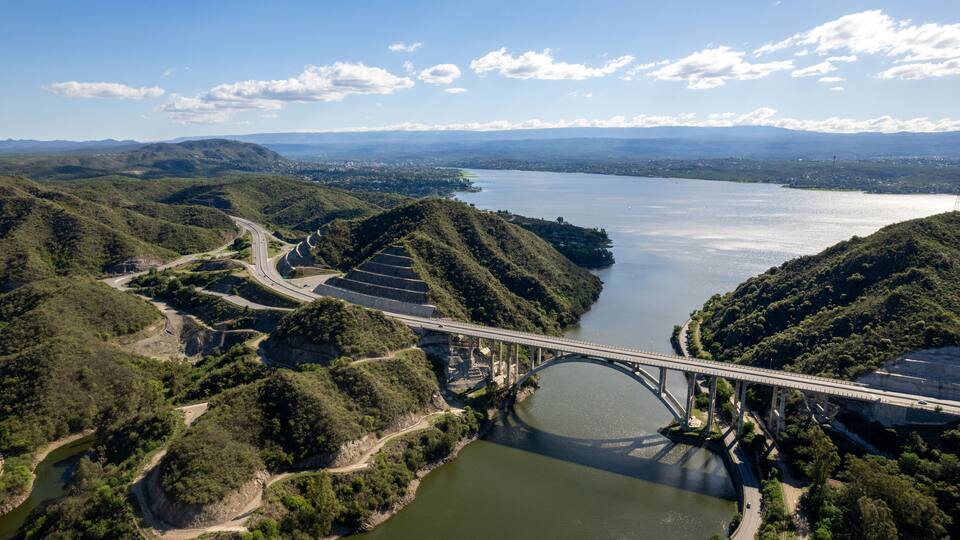 A bridge over a river, surrounded by hills and a distant cityscape.