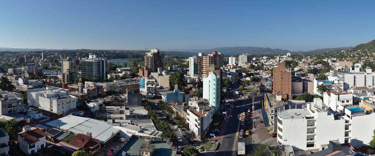 A cityscape with a mix of modern and older buildings, a busy street, and a hilly landscape in the background.