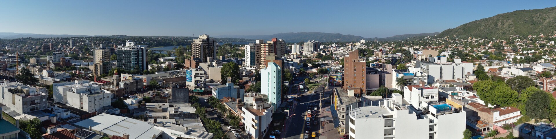 A cityscape with a mix of modern and older buildings, a busy street, and a hilly landscape in the background.