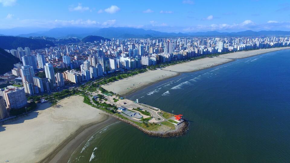 A coastal cityscape with high-rise buildings, a sandy beach, and a rocky peninsula with a park.