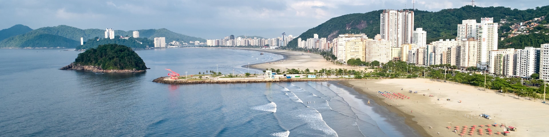 Un paisaje urbano costero con playa, una pequeña isla y edificios altos.