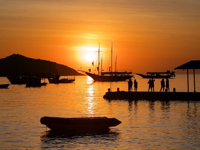 A sunset over a harbor with boats and people silhouetted against the sky.