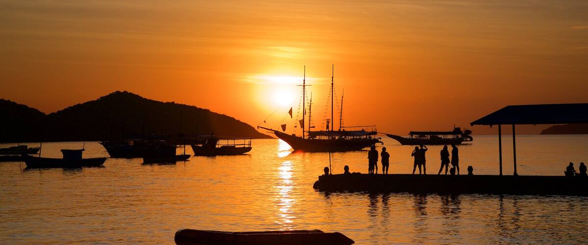 A sunset over a harbor with boats and people silhouetted against the sky.