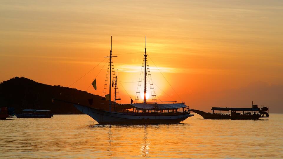 A sailing boat at sunset with a mountain in the background.