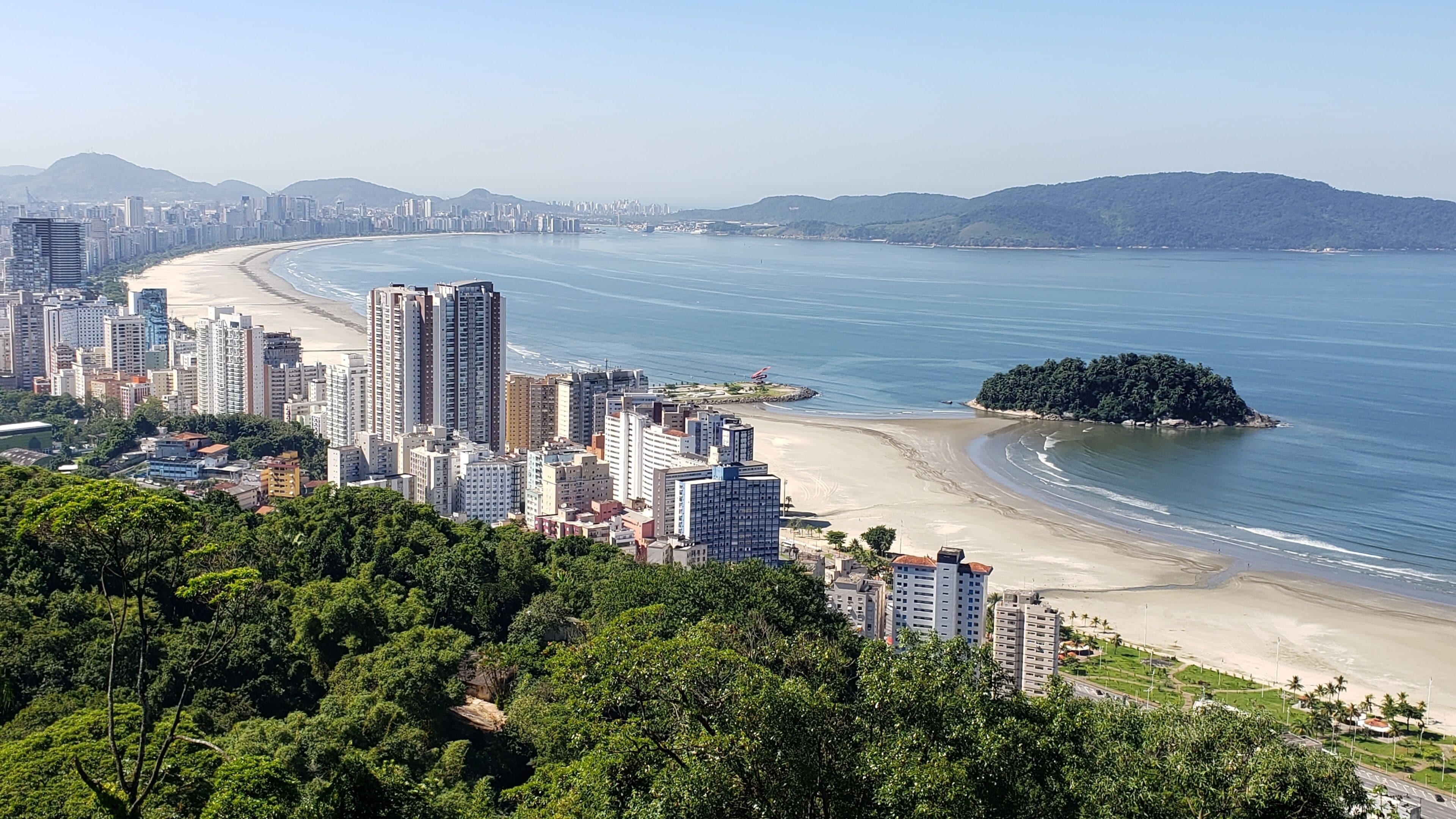 A coastal cityscape with high-rise buildings, a sandy beach, and a small island.