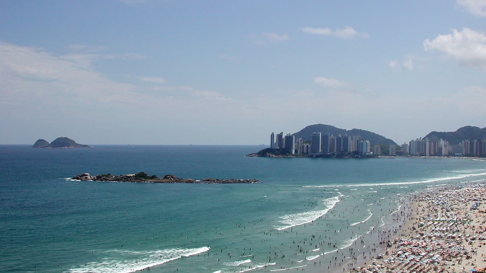 A crowded beach with a city skyline in the background.