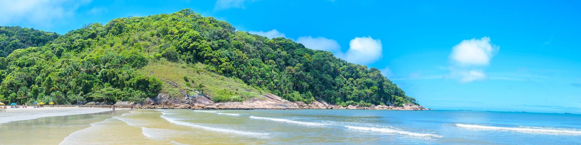 Touristic Brazilian beach on a sunny day. Panoramic view of a beach with a calm sea and few waves at Praia do Guaiuba beach - Guaruja SP Brazil.