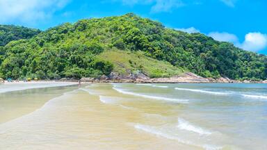 Touristic Brazilian beach on a sunny day. Panoramic view of a beach with a calm sea and few waves at Praia do Guaiuba beach - Guaruja SP Brazil.