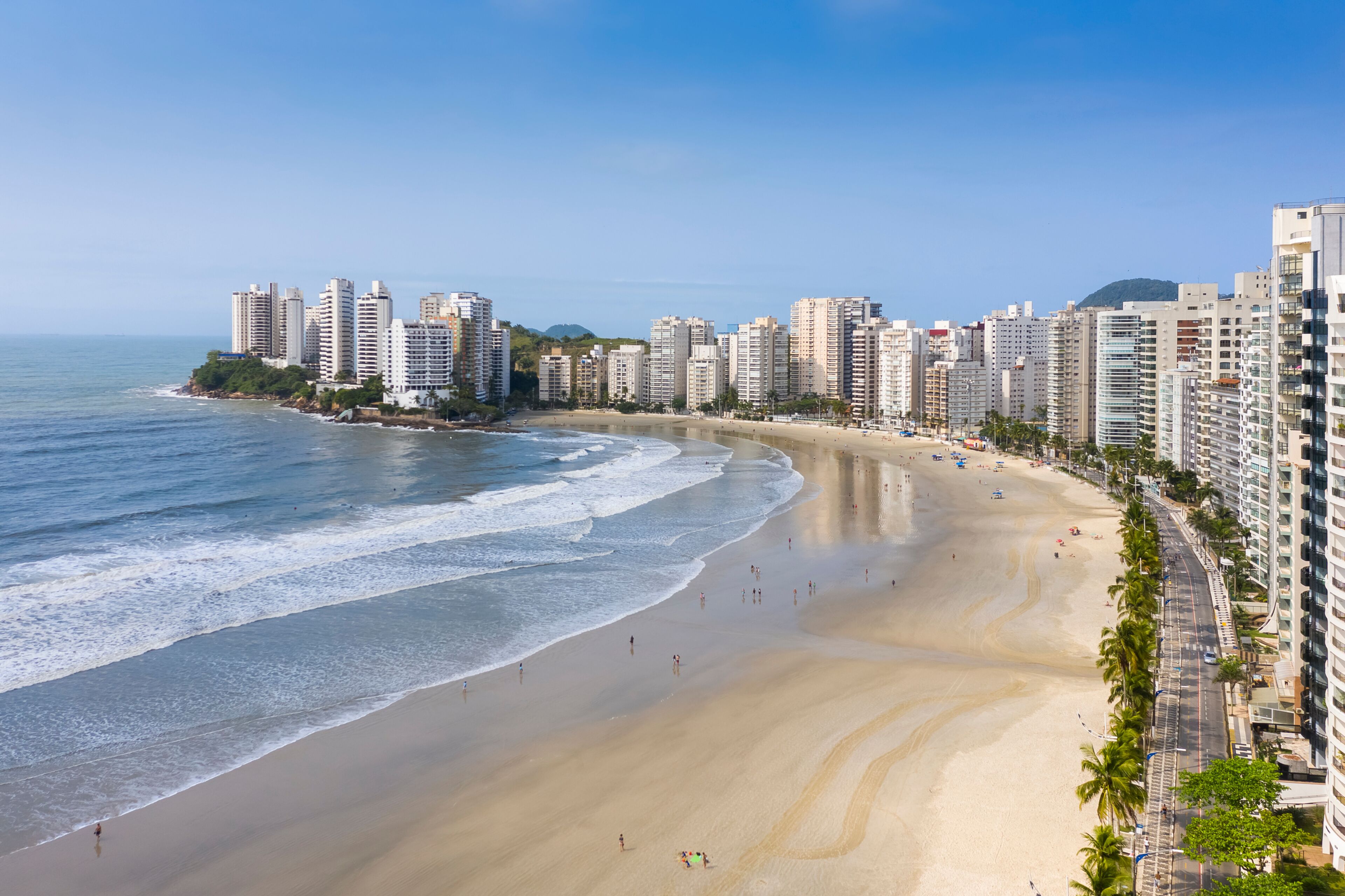 A coastal cityscape with a wide sandy beach, tall residential buildings, and a clear blue sky.