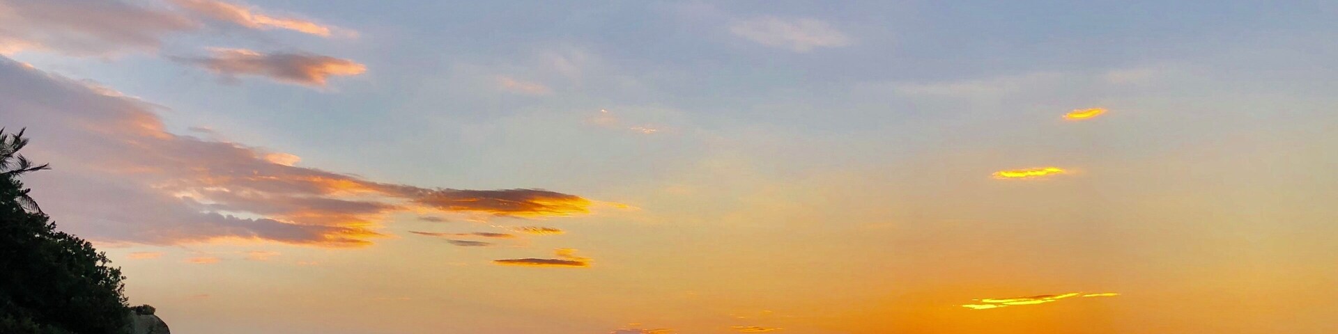 A sunset over the ocean with rocks and a distant ship.