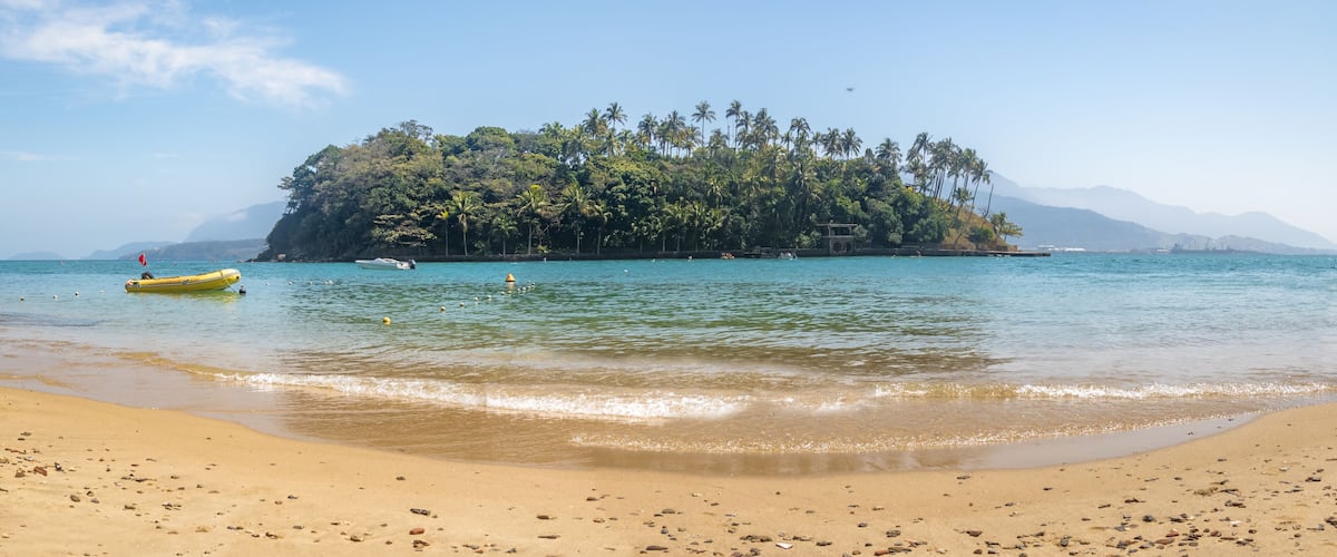 A beach with clear turquoise water, a small island with palm trees, and a yellow boat.
