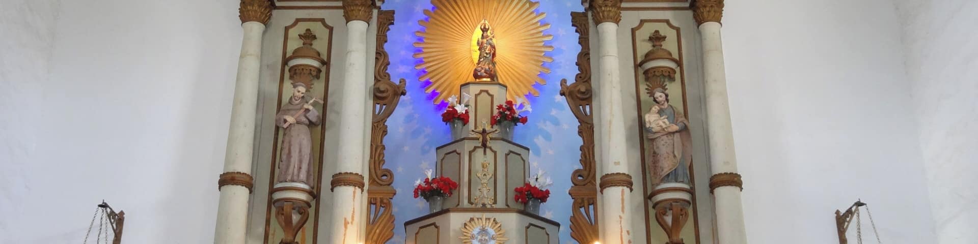 An ornate altar with a central statue, candles, and floral arrangements.