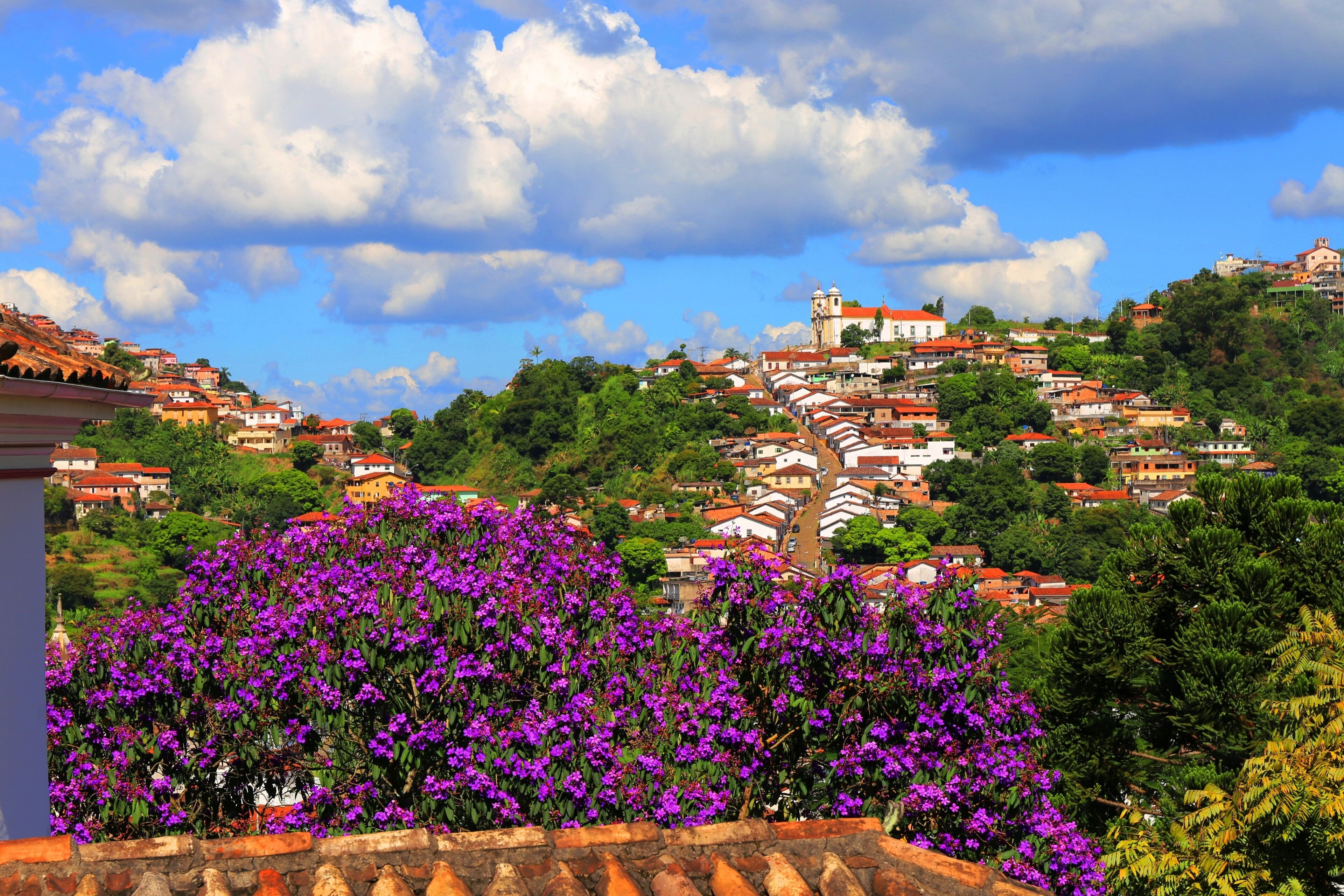 A hillside town with terracotta-roofed buildings, a prominent church with a bell tower, and lush greenery.