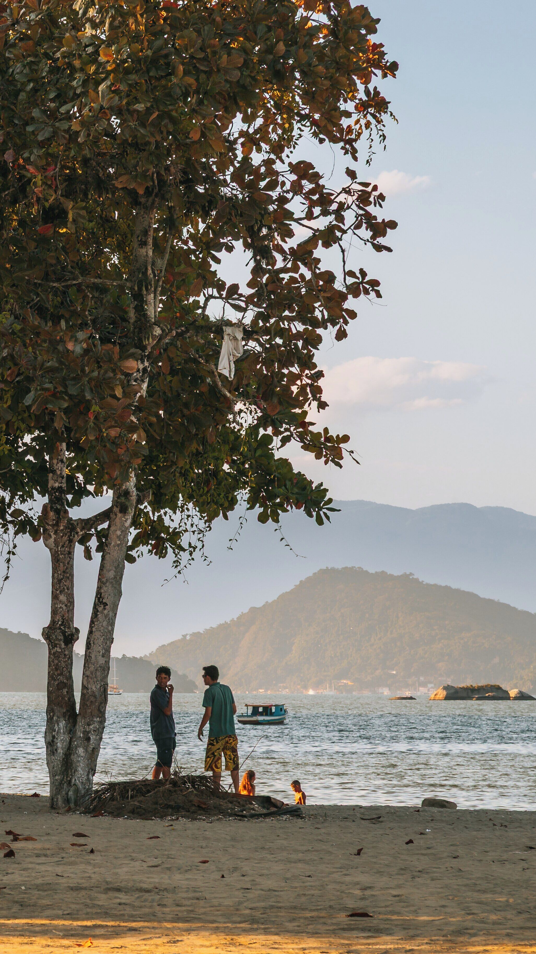 Sunset stroll along Pontal Beach in Paraty, Brazil with mountains and gentle waves in the background